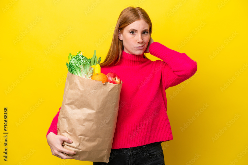 Young redhead woman holding a grocery shopping bag isolated on yellow background having doubts Young redhead woman holding a grocery shopping bag isolated on yellow background having doubts