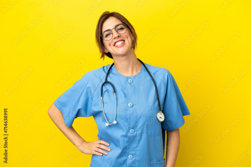 Surgeon doctor woman isolated on yellow background posing with arms at hip and smiling