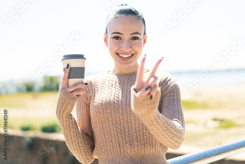 Young moroccan girl holding a take away coffee at outdoors smiling and showing victory sign