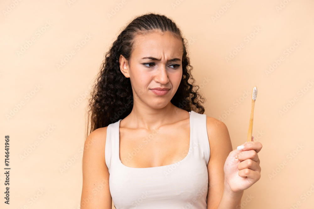 Young woman brushing teeth isolated on beige background with sad expression Young woman brushing teeth isolated on beige background with sad expression