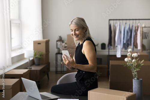 Pretty businesswoman, female designer, own brand owner working in office use smartphone, check sales on mobile application. E-business, electronic commerce, small business owner workflow in warehouse