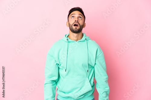 Young caucasian man isolated on pink background looking up and with surprised expression © luismolinero