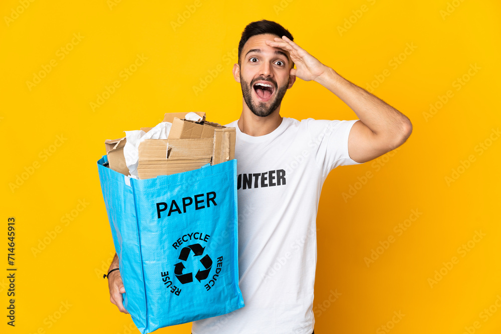 Young caucasian man holding a recycling bag full of paper to recycle isolated on white background with surprise expression Young caucasian man holding a recycling bag full of paper to recycle isolated on white background with surprise expression