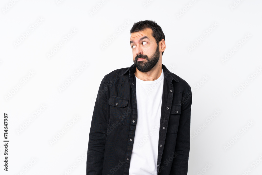 Young man with beard over isolated white background making doubts gesture looking side Young man with beard over isolated white background making doubts gesture looking side