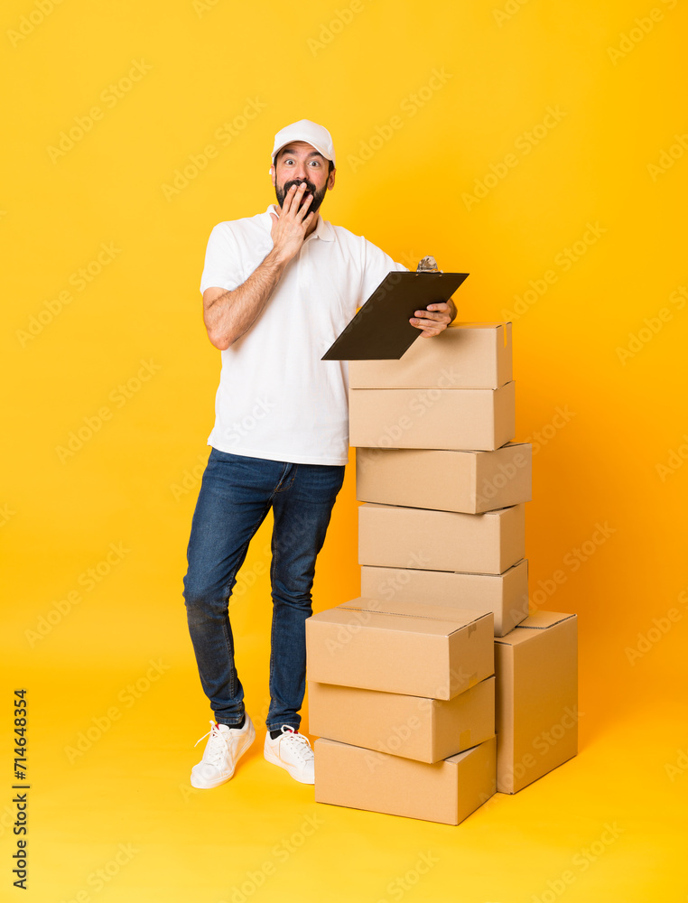 Full-length shot of delivery man among boxes over isolated yellow background Full-length shot of delivery man among boxes over isolated yellow background
