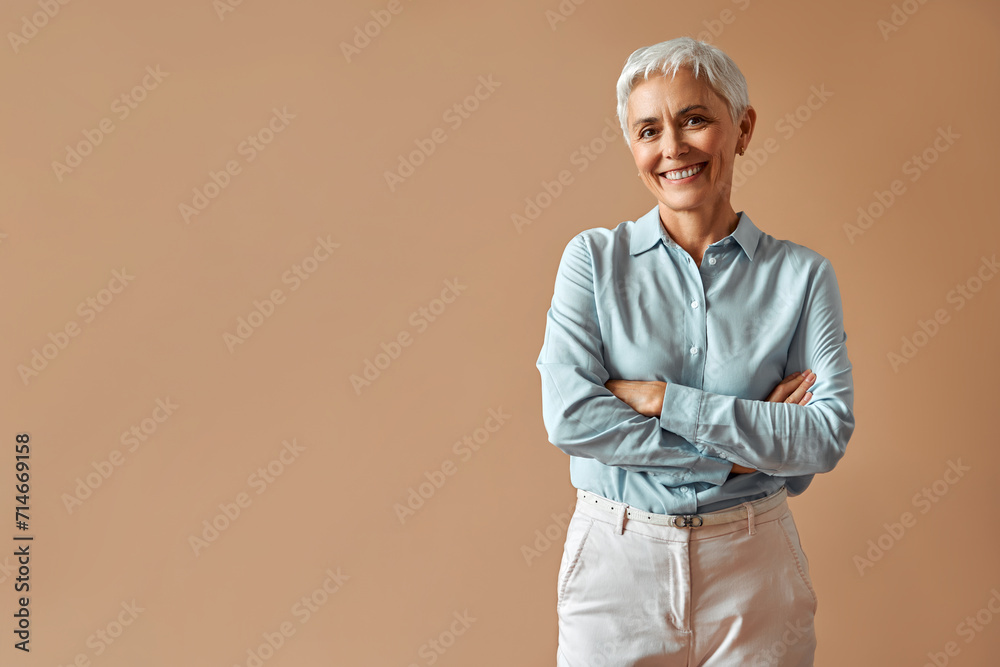 Beautiful modern mature confident smiling woman professional boss entrepreneur manager in formal wear standing on beige background and smiling with crossed arms. Business concept.