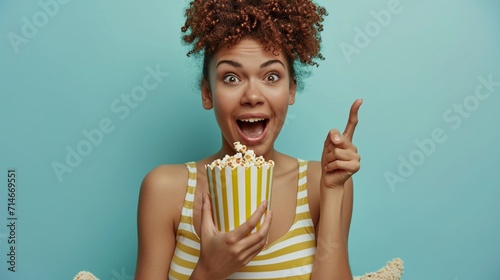Full body young woman she wearing striped tank shirt casual clothes sit in bag chair eat popcorn point index finger aside on area isolated on plain pastel light blue cyan background studio portrait. photo