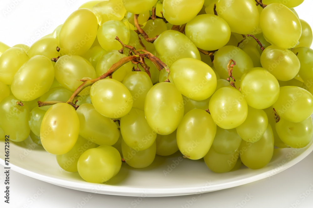 fruit composition. a large bunch of ripe green grapes lies on a white plate, close-up view fruit composition. a large bunch of ripe green grapes lies on a white plate, close-up view