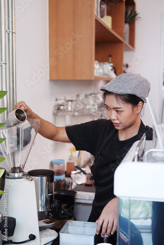 Smiling Asian Young barista woman is wearing apron and brewing coffee with machine for customers order in cafe and coffee shop. Start up small cafe business and technology Concept