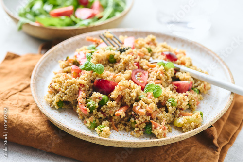 Vegan warm salad made with couscous, tomatoes, green beans, mint, roasted carrots and sweet peppers. Couscous with vegetables in bowl on light background. Variation of Tabbouleh Salad.