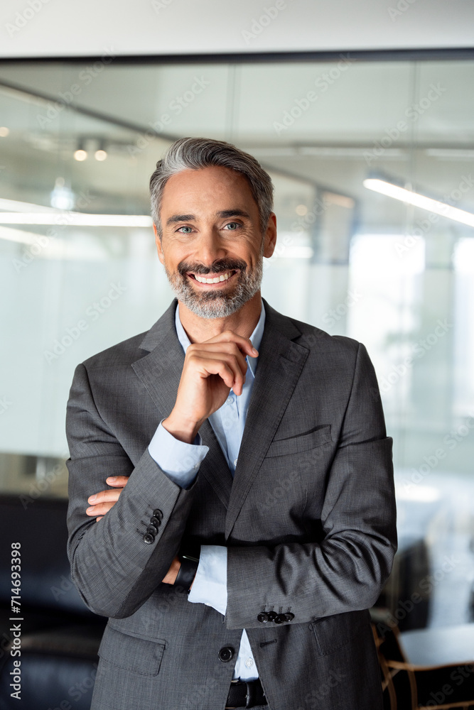 Vertical closeup portrait of handsome hispanic senior business man smiling at camera. European latin confident mature good looking middle age leader male businessman standing on blur office background Vertical closeup portrait of handsome hispanic senior business man smiling at camera. European latin confident mature good looking middle age leader male businessman standing on blur office background