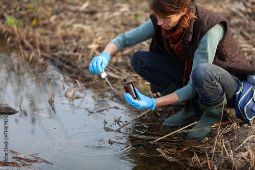 Adult Caucasian Woman Biologist Working on Field Checking Mechanical Pollution of Water Pond in City Park photo