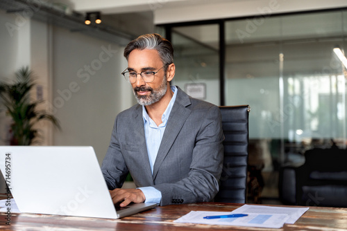 Happy mature European business man ceo trader using computer, typing, working in modern office, doing online data market analysis, thinking planning tech strategy looking at laptop with copy space.