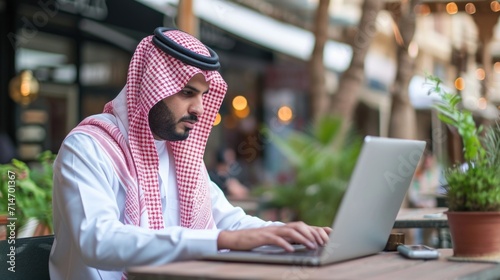 Saudi Arab business man on laptop working outdoor wearing traditional dress. Muslim businessman from Saudi Arabia typing photo