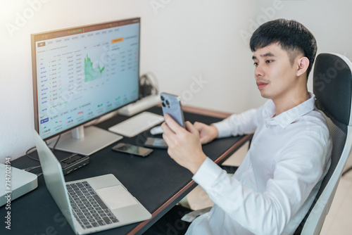 Handsome young businessman is trading the stock market via computer and smartphone.