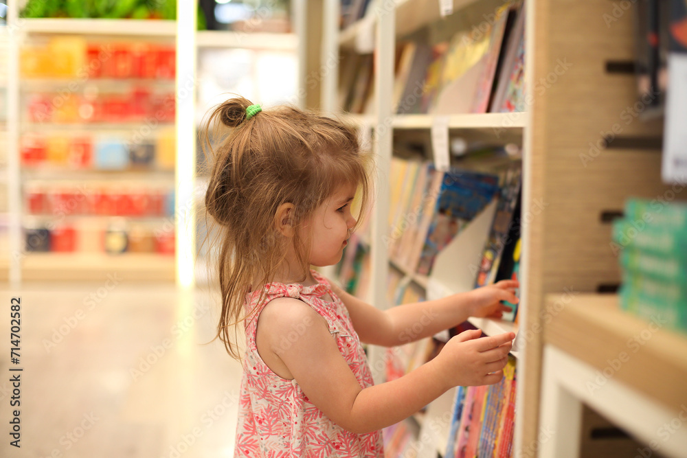 Little cute child picking books from the bookshelf Little cute child picking books from the bookshelf