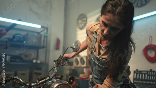 Young woman wipes vintage retro motorbike. Beautiful repair woman inspecting condition of motorcycle. Maintenance and repairing concept. Biker girl lifestyle. Creative authentic workshop. photo