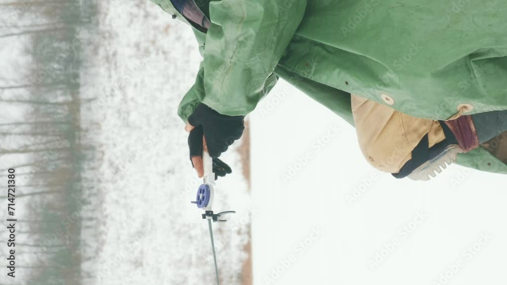 Man in winter extreme clothes is catching fish on frozen lake. Vertical video Man in winter extreme clothes is catching fish on frozen lake. Vertical video