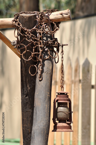 Old and aged lamp hanging from a stick with rusty chains, corroded antique objects