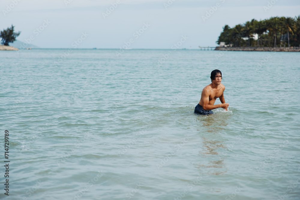 Happy Asian Man Swimming in the Tropical Ocean, Enjoying Vacation on the Beach
