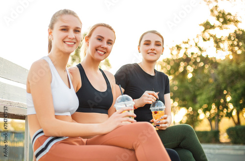 Young sportswoman with fresh drink sitting near friends
