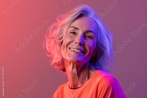 A woman with gray hair is smiling and wearing an orange shirt