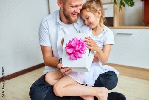 Smiling Father and Daughter Sharing a Gift Box With a Pink Bow Indoors