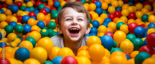 Laughing boy close-up having fun in a ball pit at a children's amusement park and indoor play center, laughing, playing with colorful balls in a ball pit at a playground. Banner. photo