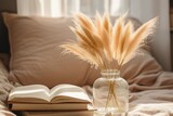 Dry pampas grass flowers in a glass vase on a tablet on a coffee table next to a bed on a sunny day, beige colored pillows and cushions, boho style