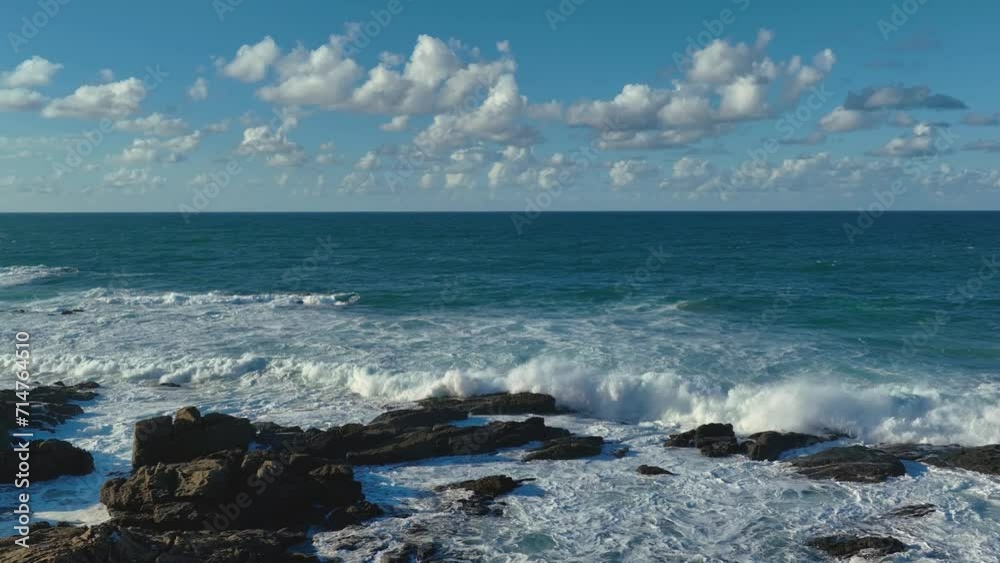 Slow motion drone shot of the sea waves crashing on the rock formations on the shore on a sunny day Slow motion drone shot of the sea waves crashing on the rock formations on the shore on a sunny day