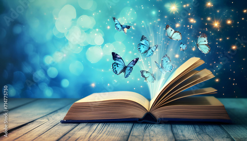 Open book with magic light and glowing butterflies flying out of it on wooden table against light blue bokeh background