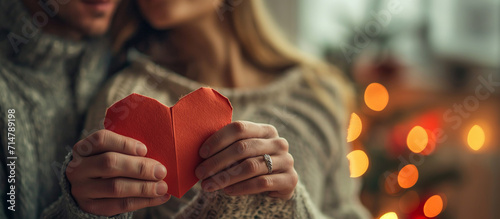 Happy Valentine's Day. Couple holding a paper heart with focus on hands, bokeh lights in background.