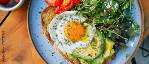 A hearty breakfast served: sunny-side-up egg on toast with sliced avocado, a side of greens, and fresh tomatoes