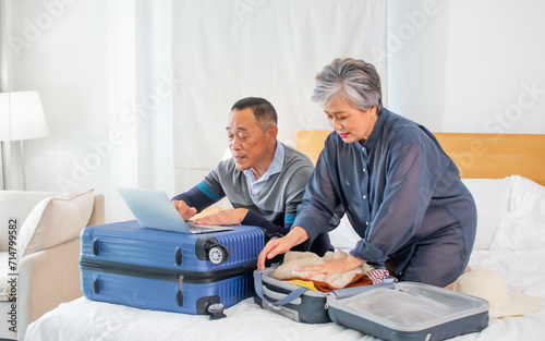 Asian sweet senior elderly couple wearing casual clothes, sitting on bed, packing luggages, planning for traveling after retirement, smiling with happiness. Lifestyle, Healthcare Concept.
