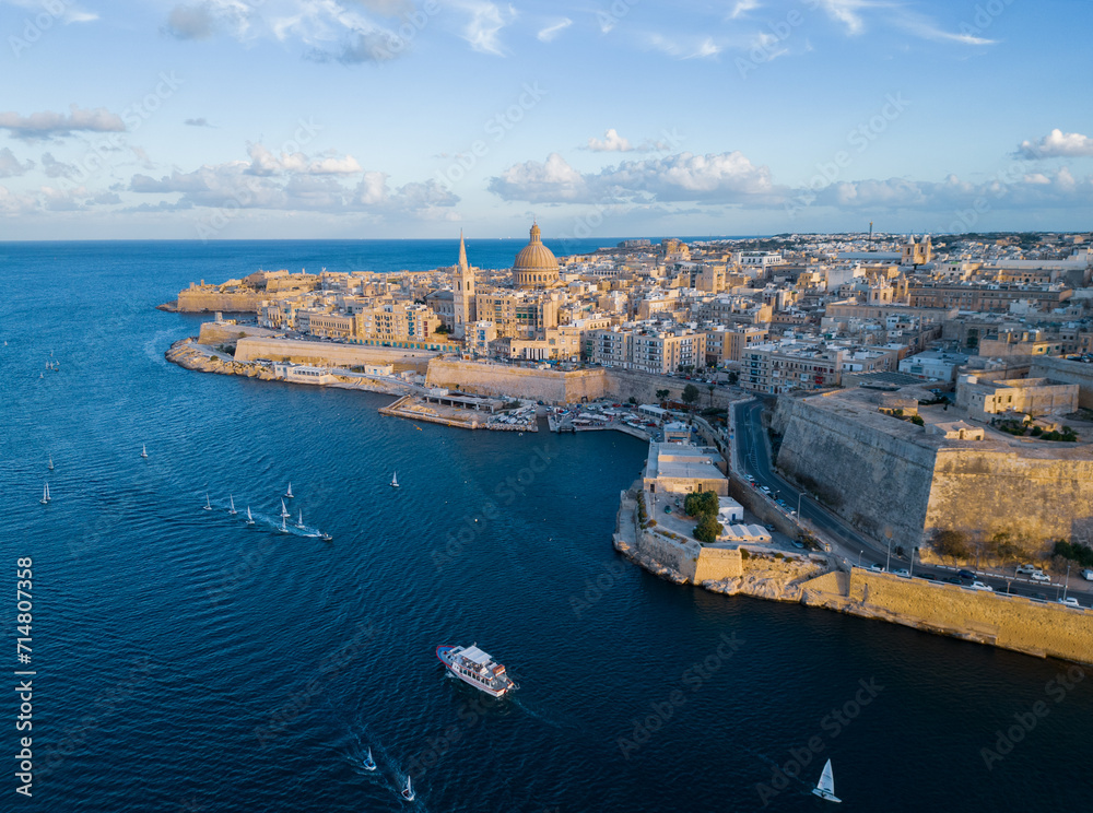 Valletta old town with cathedral at golden sunset.  Aerial view on historic city with sailing boats returning into harbor. Malta at the end of summer season.