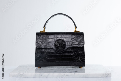 Luxury fashion black handbag made of crocodile skin, on marble and white background