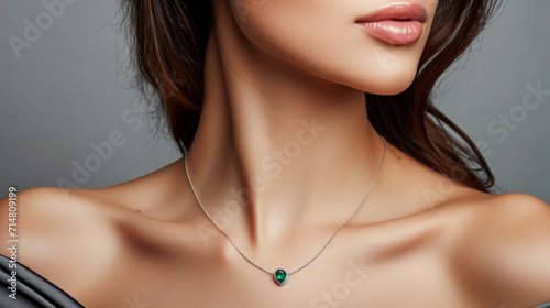 sensual model wearing a delicate necklace with an emerald, green pendant, closeup isolated on grey background