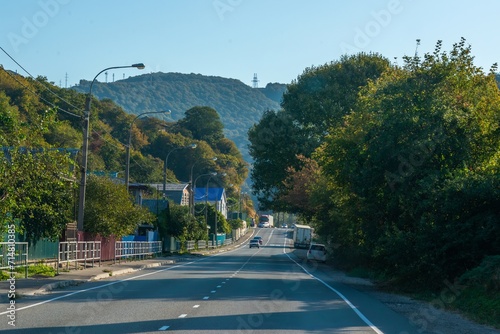 Fototapeta Naklejka Na Ścianę i Meble -  M4-Don highway in the mountains of the Western Caucasus (South Russia), passing through a small village, surrounded by a green deciduous forest with tall trees on a sunny summer day