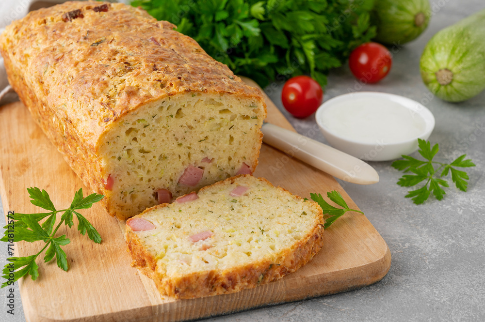 Zucchini bread with cheese, ham and fresh herbs on a wooden board on a gray background. Healthy food.