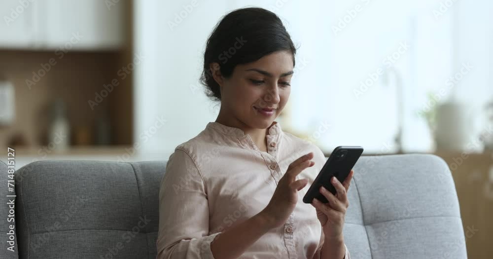 Positive pretty Indian woman using online app on smartphone for communication, sitting on home couch, typing message, chatting, getting cheerful, smiling, turning look away, thinking Positive pretty Indian woman using online app on smartphone for communication, sitting on home couch, typing message, chatting, getting cheerful, smiling, turning look away, thinking