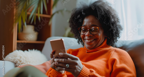 african american woman smiling looking at phone on the sofa at home   © Yi_Studio