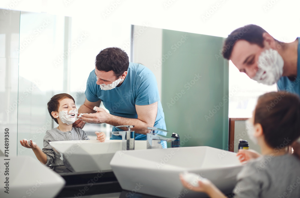 Young father and little son applying shaving foam on face in bathroom at the morning together near the mirror Young father and little son applying shaving foam on face in bathroom at the morning together near the mirror