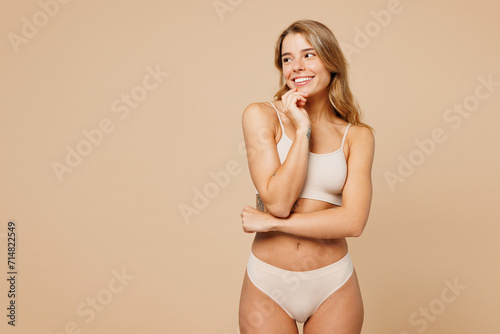 Young happy nice lady woman with slim body perfect skin wears nude top bra lingerie stand prop up chin look aside on area isolated on plain pastel light beige background. Lifestyle diet fit concept.