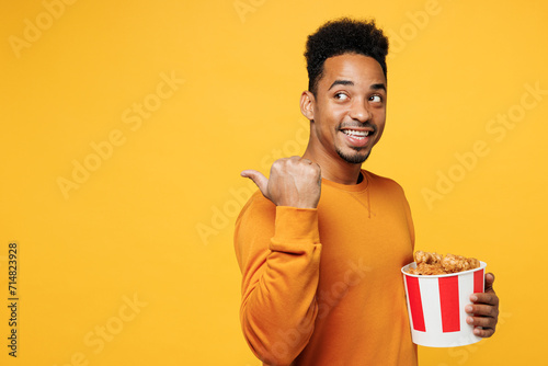 Young man he wear sweatshirt casual clothes hold takeaway bucket of chicken nuggets point finger back isolated on plain yellow background. Proper nutrition healthy fast food unhealthy choice concept. © ViDi Studio