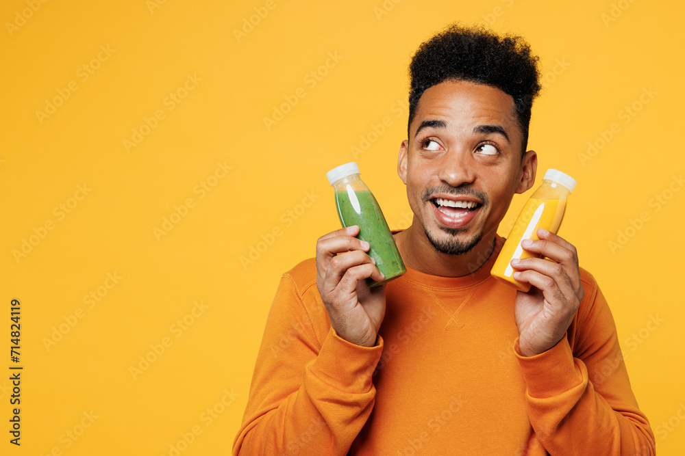 Young man wear casual clothes hold show fruit juice green vegetable smoothie as detox diet look aside isolated on plain yellow background. Proper nutrition healthy fast food unhealthy choice concept. Young man wear casual clothes hold show fruit juice green vegetable smoothie as detox diet look aside isolated on plain yellow background. Proper nutrition healthy fast food unhealthy choice concept.