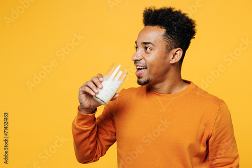 Young smiling fun happy man wear orange sweatshirt casual clothes isolated on plain yellow hold in hand glass drink regular milk background Proper nutrition healthy fast food unhealthy choice concept