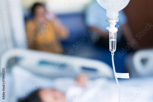 Close up set iv fluid intravenous drop saline drip in hospital room with blurry patient woman and caregiver on hospital bed.Medical treatment emergency patient.Caregiver and hopeful concept. photo