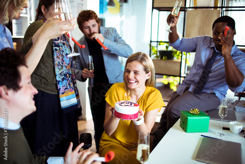 Young smiling woman holding birthday cake with colleagues in office