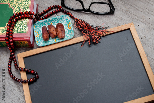 A thoughtfully arranged scene capturing the essence of Ramadan. Empty space of the black chalkboard for text and messages. Rosary beads rests beside a plate of dates, symbolizing the traditional break photo