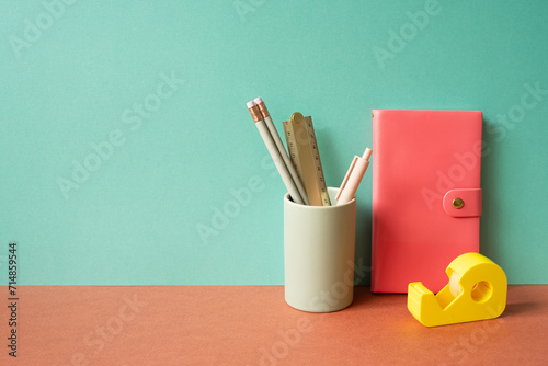 Obraz na płótnie Pink diary notebook and writing supplies stationery in holder on red desk. mint green wall background w salonie